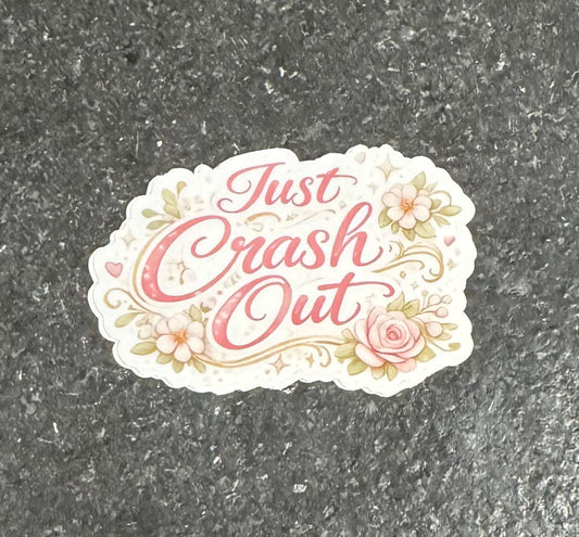May include: A sticker with the phrase "Just Crash Out" in a cursive font, surrounded by floral and decorative elements. The text and accents are in shades of pink and gold, with a white background.